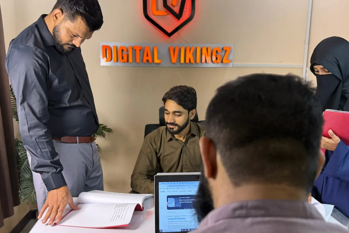Digital Vikingz team members reviewing a document and a laptop under the Digital Vikingz sign in the office